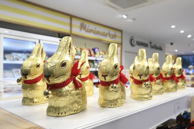 Un expositor con muchos conejos de chocolate envueltos en un packaging de oro con bufanda roja.