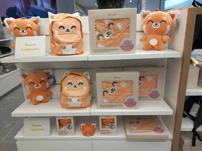 Expositor con una colección de bonitos artículos de temática zorro naranja, como peluches, mochilas y toallas. Un cartel en el que pone «Nueva Colección».