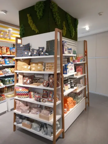 Un escaparate presenta textiles coloridos y artículos para el hogar en estantes blancos con soportes de madera. El ambiente es luminoso, moderno y acogedor.
