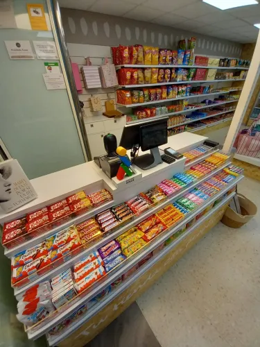 Mostrador de tienda con una amplia variedad de barras de chocolate y snacks cuidadosamente presentados. Los estantes al fondo ofrecen papas fritas de colores y más snacks.