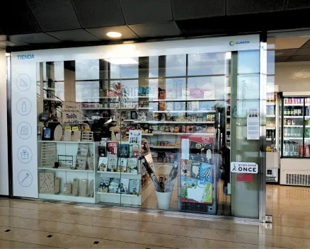 Se muestra la entrada de la tienda ILUNION Tu Tienda. Se puede observar una nevera con bebidas, regalos, libros y mucho más