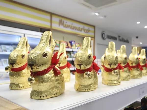 Un expositor con muchos conejos de chocolate envueltos en un packaging de oro con bufanda roja.