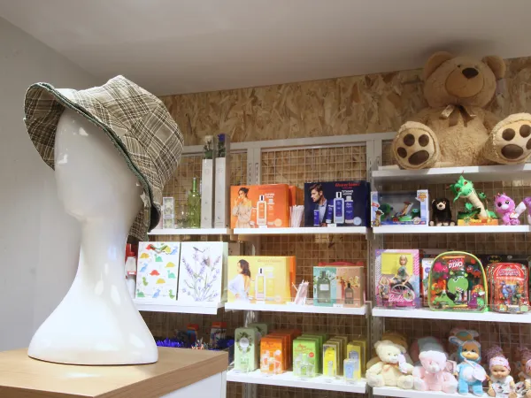 Una cabeza de maniquí con sombrero a cuadros se exhibe sobre un pedestal de madera. Detrás, unas estanterías repletas de juguetes de colores, juegos y grandes osos de peluche crean un ambiente lúdico.