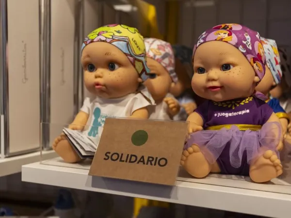 Un expositor de muñecas de colores vestidas con diversos trajes, con un cartel que pone «SOLIDARIO» bien visible delante.