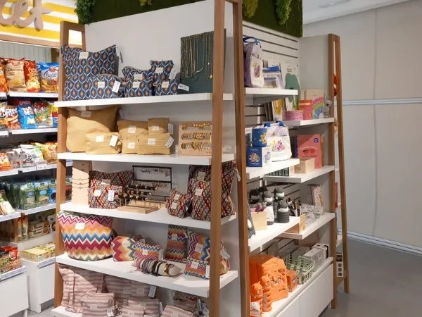 Un escaparate presenta textiles coloridos y artículos para el hogar en estantes blancos con soportes de madera. El ambiente es luminoso, moderno y acogedor.