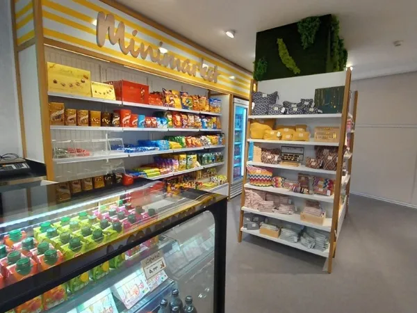 Un minimercado bien iluminado con estanterías coloridas. Se exhiben refrigerios, bebidas, artículos para el hogar y textiles, creando un ambiente acogedor.