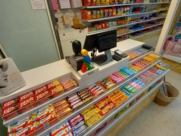 Mostrador de tienda con una amplia variedad de barras de chocolate y snacks cuidadosamente presentados. Los estantes al fondo ofrecen papas fritas de colores y más snacks.